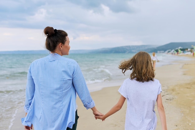 Gelukkige moeder en dochter wandelen op het strand aan zee, hand in hand achteraanzicht