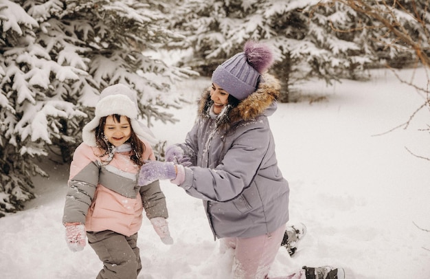 Gelukkige moeder en dochtertje spelen sneeuwballen in een besneeuwd natuurpark in een sneeuwval. Geweldig leuk moment. Tijd samen doorbrengen op een mooie koude winterdag.