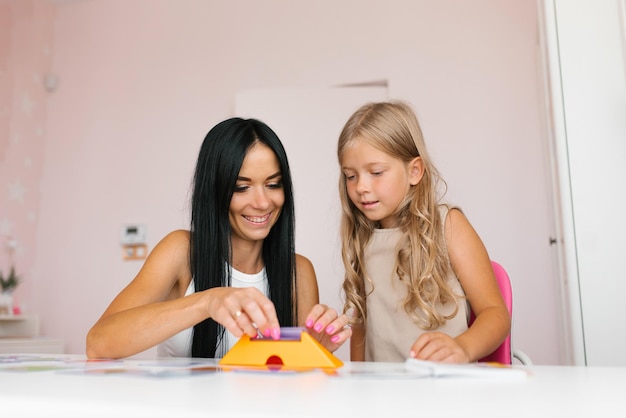 Gelukkige moeder en een dochtertje hebben plezier met het spelen van een logisch spel samen aan tafel een gelukkige moeder en een nieuwsgierig meisje houden zich bezig met educatieve activiteiten die thuis vrije tijd doorbrengen