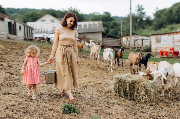 Gelukkige moeder en haar dochter brengen tijd door op een eco-boerderij tussen geiten.