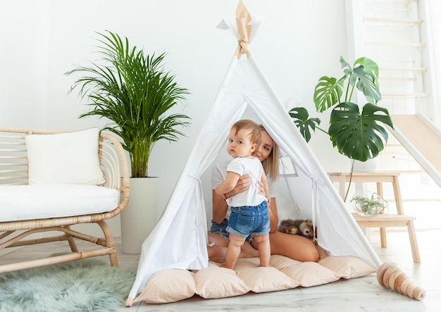 Foto gelukkige moeder en haar kleine dochter spelen thuis in een wigwam.