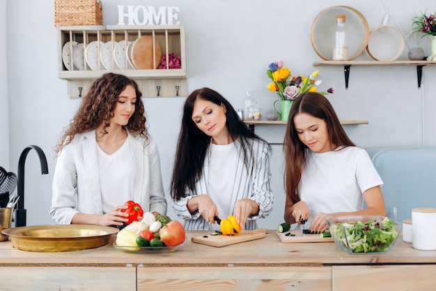 Gelukkige moeder en haar leuke dochters die groenten in de keuken snijden.