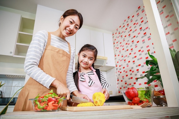 Gelukkige moeder en kind die gezond voedsel bereiden en thuis plezier hebben in de keuken