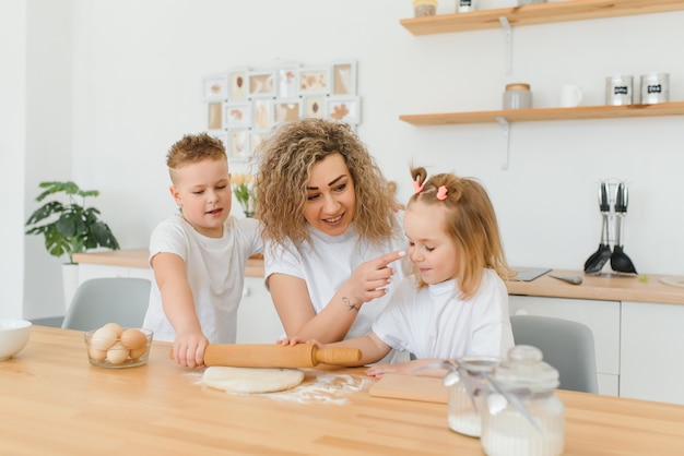 Gelukkige moeder en kinderen mengen ingrediënten voor zelfgemaakte cake, taart of koekjesdeeg in de keuken.