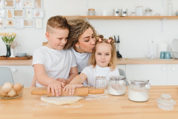 Gelukkige moeder en kinderen mengen ingrediënten voor zelfgemaakte cake, taart of koekjesdeeg in de keuken.