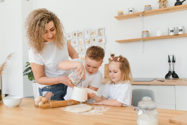 Gelukkige moeder en kinderen mengen ingrediënten voor zelfgemaakte cake, taart of koekjesdeeg in de keuken.
