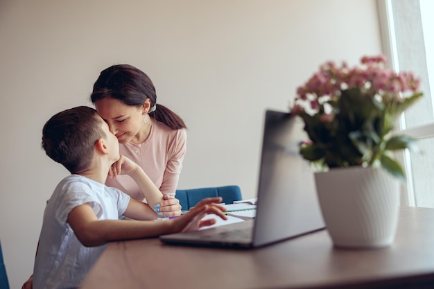 Gelukkige moeder en kleine tienerzoon die thuis neus aan neus knuffelen terwijl ze online leren