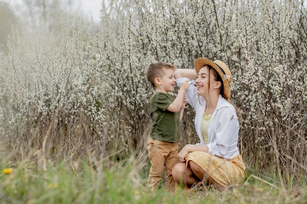 Gelukkige moeder en zoon die samen plezier hebben. moeder knuffelt zachtjes haar zoon. op de achtergrond bloeien witte bloemen. moederdag.