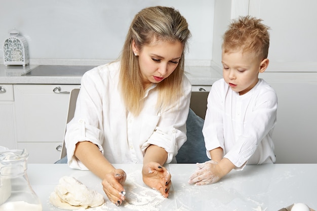 Gelukkige moeder en zoon veel plezier met koken in een witte keuken aan tafel