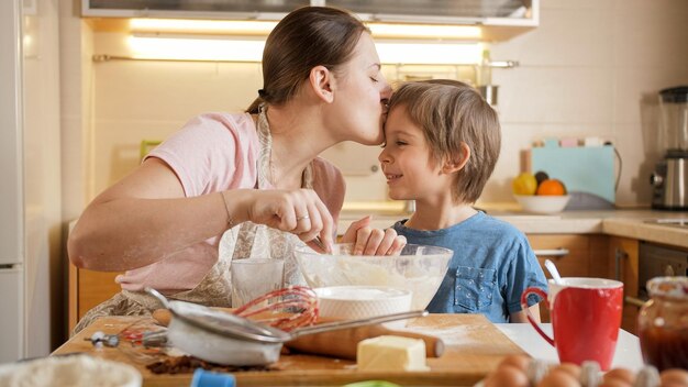 Foto gelukkige moeder kuste haar lachende zoon tijdens het koken op de keuken