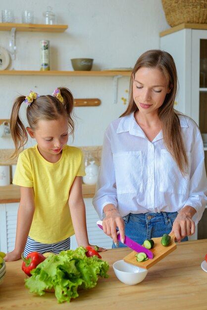 Gelukkige moeder leert dochtertje gezond eten te koken moeder en meisje lachend praten