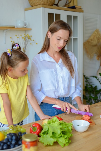 Gelukkige moeder leert dochtertje gezond eten te koken moeder en meisje lachend praten