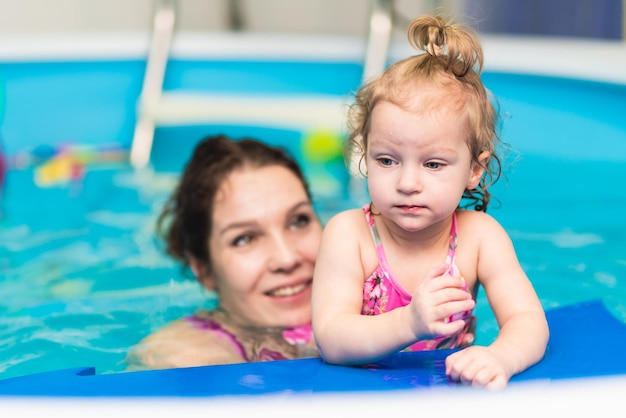 Gelukkige moeder leert haar dochtertje zwemmen in het zwembad