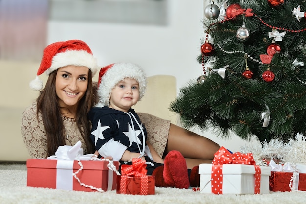 Gelukkige moeder met een kleine jongen in de buurt van een kerstboom. nieuwjaarsgeschenken