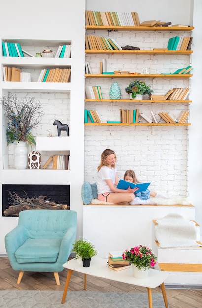 Gelukkige moeder met haar dochter die een boek leest en glimlacht terwijl ze op de vloer in de woonkamer zit