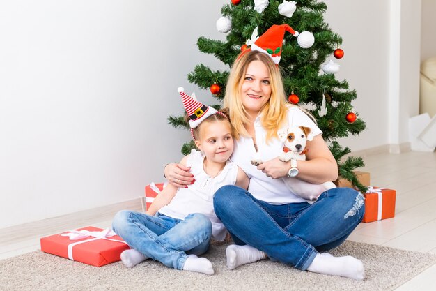 Gelukkige moeder met haar dochter en jack russell terrier-hond die bij de kerstboom zit