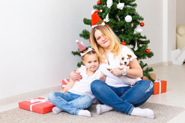 Gelukkige moeder met haar dochter en jack russell terrier-hond die bij de kerstboom zit