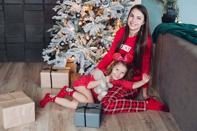 Gelukkige moeder met haar dochtertje in de buurt van de kerstboom met geschenken