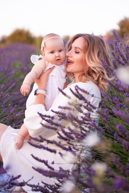 Gelukkige moeder met mooie dochter op lavendelachtergrond. Mooie vrouw en schattige baby zitten in m