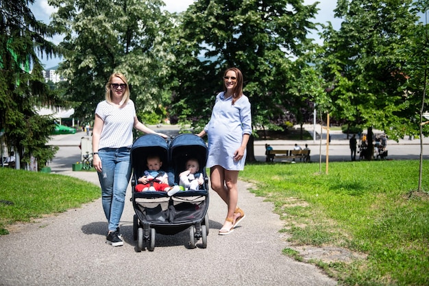 Gelukkige moeder met vriend wandelende kinderwagen in park