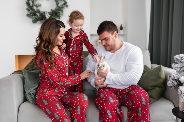 Gelukkige moeder, vader en dochter verheugen zich over het witte pluizige konijn De ochtend voor Kerstmis