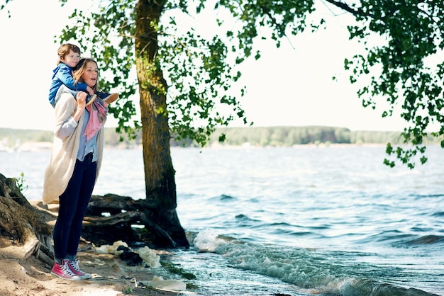 Foto gelukkige moeder zorgt voor haar jonge zoon en loopt in de zomer langs de oever van het meer in het park
