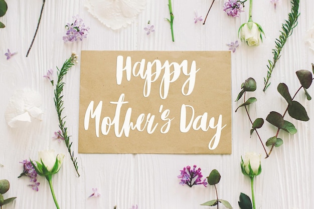 Foto gelukkige moederdag gelukkige moederdag tekst op papieren kaart en lila rozen eucalyptus bloemen samenstelling op wit hout plat leggen stijlvolle bloemenwenskaart handgeschreven letters moederdag