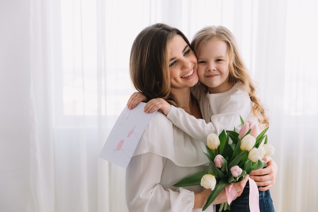 Gelukkige moederdag. kind dochter feliciteert moeders en geeft haar een briefkaart en bloemen tulpen.