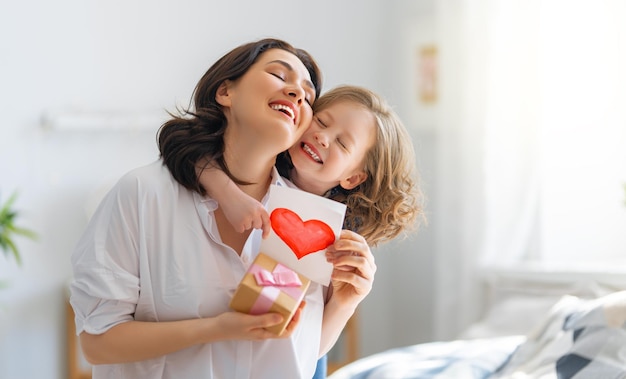 Gelukkige moederdag! kinddochter feliciteert moeder en geeft haar een ansichtkaart. moeder en meisje glimlachen en knuffelen. familie vakantie en samenzijn.