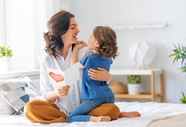 Gelukkige Moederdag! Kinddochter feliciteert moeder en geeft haar een ansichtkaart. Moeder en meisje glimlachen en knuffelen. Familie vakantie en samenzijn.