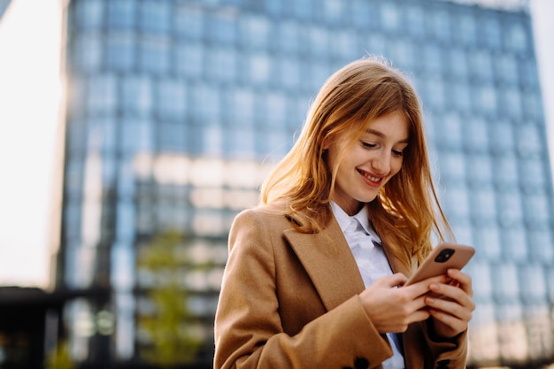Foto gelukkige mooie brunette meisje gebruikt mobiele telefoon in de buurt van het kantoor mooie vrouw browsen telefoon terwijl