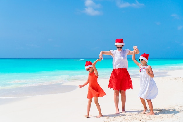 Gelukkige mooie familie van moeder en kinderen in rode kerstmuts op een tropisch strand vieren kerstmis