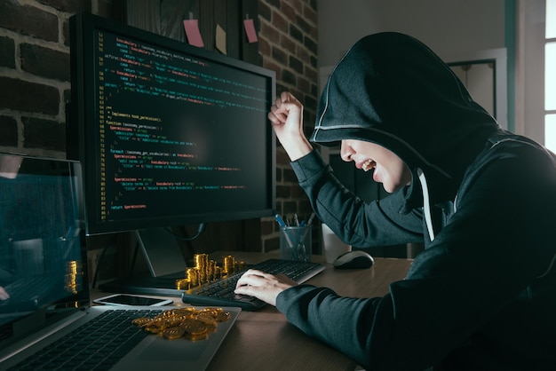 Foto gelukkige mooie hacker hief handviering succesvol op toen ze het slechte gegevensvirus afmaakte en veel bitcoin op het bureau liet zien.