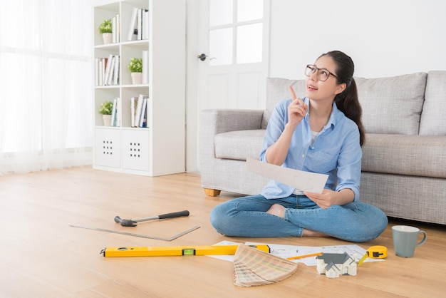 gelukkige mooie huisvrouw met nieuw huis interieur schetspapier dagdromen en denken goed idee maken van wijzend gebaar zittend in de houten vloer van de woonkamer.