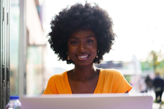 Gelukkige mooie jonge zwarte vrouw met een laptop in een café.
