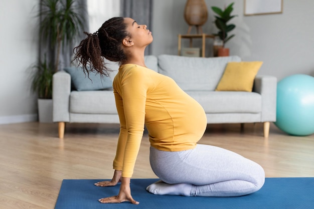 Gelukkige mooie jonge zwarte zwangere vrouw met grote buik die oefeningen doet die yoga beoefenen in de woonkamer