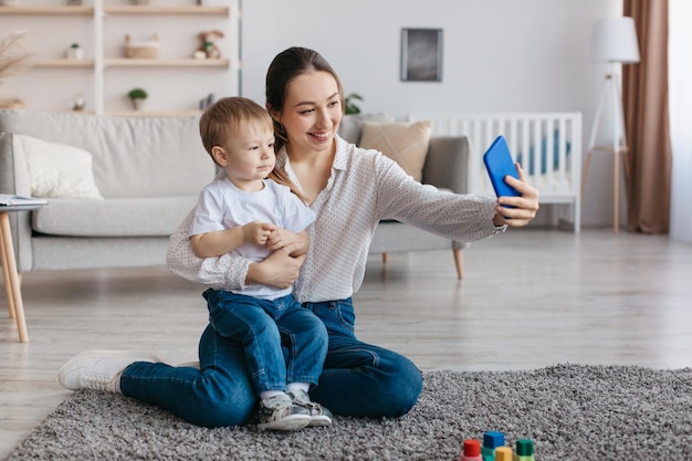 Gelukkige mooie moeder die selfie maakt met haar schattige peuterzoonmoeder die foto's maakt op smartphone