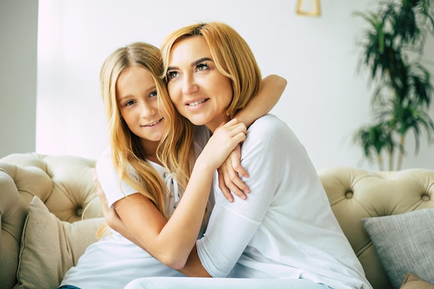 Gelukkige mooie moeder en dochter die tijd samen doorbrengen, knuffelen en plezier hebben terwijl ze thuis op de bank zitten. Familie concept