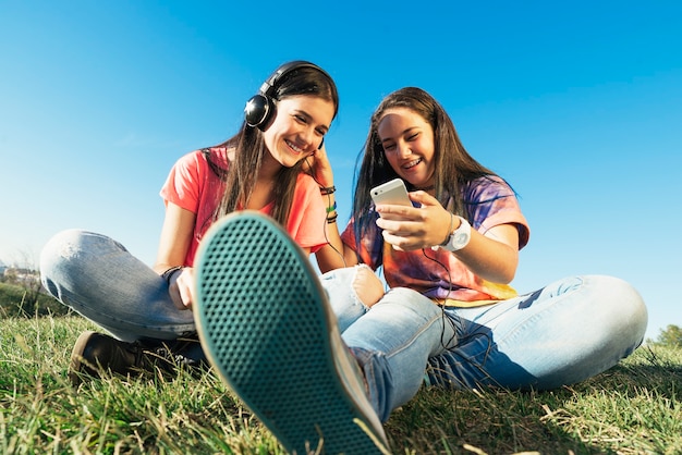 gelukkige mooie tienervrienden in het zomerpark die muziek luisteren.