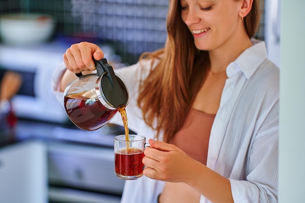 Gelukkige mooie vrolijke zorgeloze tevreden aantrekkelijke vrouw die hete zwarte thee drinkt in de keuken thuis