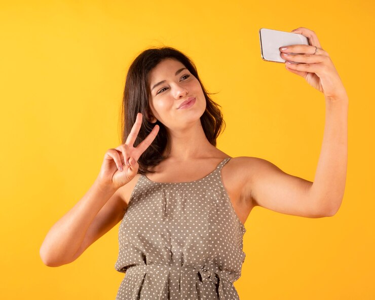 Gelukkige mooie vrouw die foto met mobiele telefoon, gele achtergrond maakt