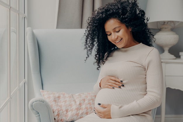 Gelukkige mooie zwangere vrouw in vrijetijdskleding die teder buik omhelst