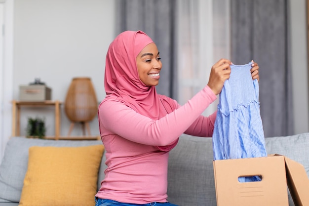 Gelukkige moslim shopaholic dame ontvangt nieuwe outfit van winkel die kartonnen doos uitpakt enthousiast over