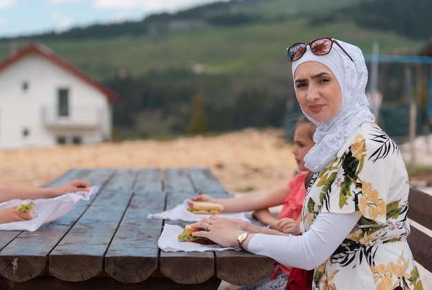 Gelukkige moslimfamilie die aan een tafel in het park eet tijdens het picknicken op de zomervakantie