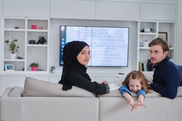 Gelukkige moslimfamilie die samen tijd doorbrengt in een modern huis. Ouders spelen met dochter op de bank tijdens de ramadan. Traditionele modieuze Arabische kleding.