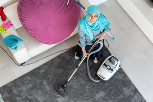 Gelukkige moslimvrouw die moderne huiswoonkamer schoonmaakt. Foto van hoge kwaliteit