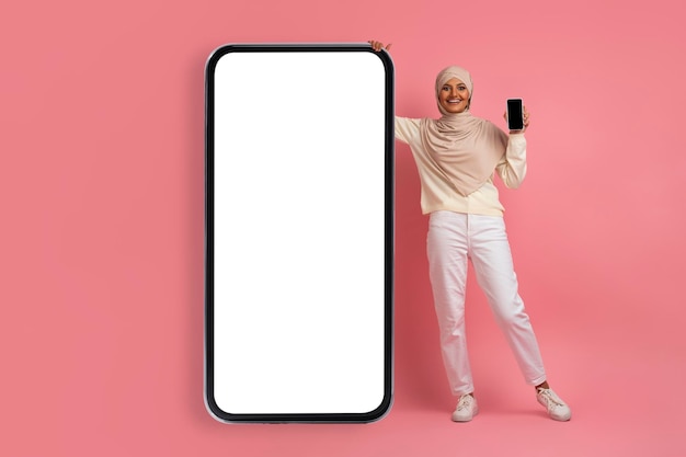 Gelukkige moslimvrouw in hijab die zich dichtbij grote lege smartphone bevindt