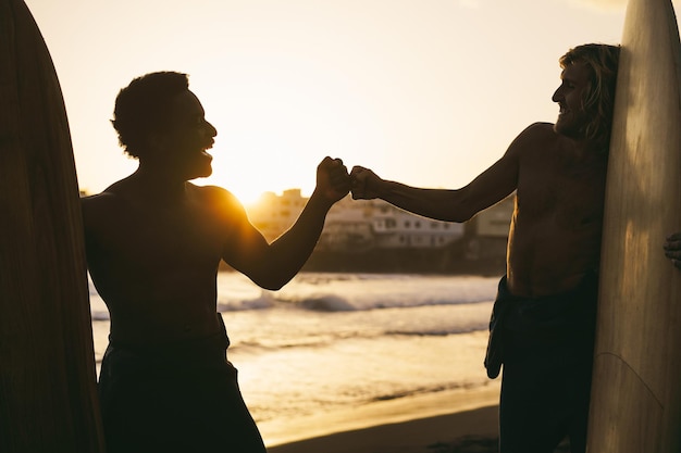 Gelukkige multiraciale surfers die plezier hebben op het strand na een surfsessie Focus op vuisten