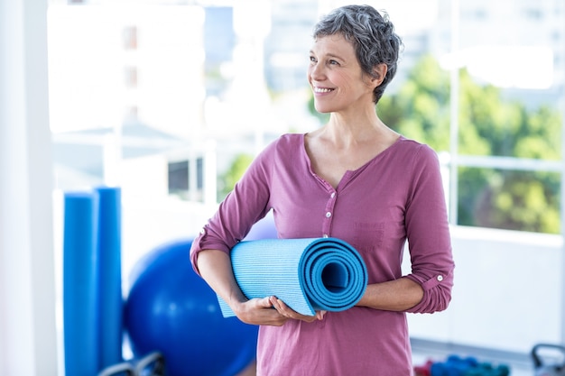 Gelukkige nadenkende rijpe vrouw met yogamat