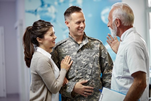 Gelukkige officier en zijn vrouw communiceren met senior arts terwijl ze in een gang in de medische kliniek staan